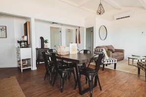 A dining area with a wooden table and chairs, a kitchen area with a coffee machine, and a living area with a sofa and a round mirror. - The Lazy Days Main Cottage - Lakefront (Lambton Shores)