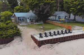 A beachside cabin with a deck, outdoor seating, and a sandy area. - The Lazy Days Main Cottage - Lakefront (Lambton Shores)