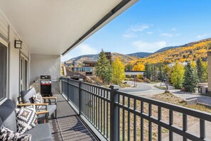 A balcony with outdoor furniture, a grill, and a view of a town with autumn-colored trees and hills. - Modern Western Luxury in Lionshead, 2min walk to Gondola, Hot Tubs & Ski Locker (Vail)