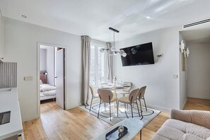 A modern living room with a dining area, a TV mounted on the wall, and a sofa. - Charming 2BDR AC Le Marais Centre de Paris (Paris)