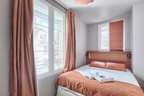 A hotel room with a bed, a window with curtains, a view of buildings outside, and a small window above the bed. - Charming 2BDR AC Le Marais Centre de Paris (Paris)