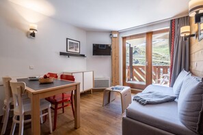 Ein gemütliches Zimmer mit einem Holztisch, roten Stühlen, einer Couch und einem Fernseher an der Wand.