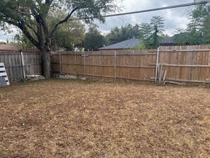 A fenced backyard with dry grass, a tree, and a wooden fence. - Cozy 2-bedroom duplex in awesome Dallas and close to downtown Dallas (Dallas)