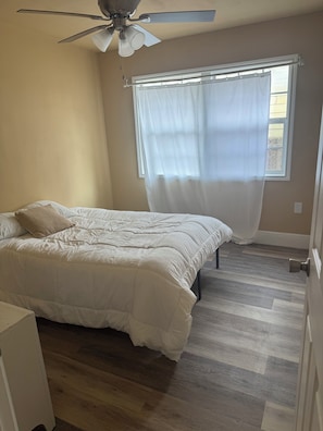 A bedroom with a bed, a ceiling fan, a window with curtains, and a wooden floor. - Cozy 2-bedroom duplex in awesome Dallas and close to downtown Dallas (Dallas)