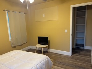 Ein Schlafzimmer mit einem Bett, einem Fernseher auf einem kleinen Tisch, einem Schrank und einer Tür zu einem anderen Raum.