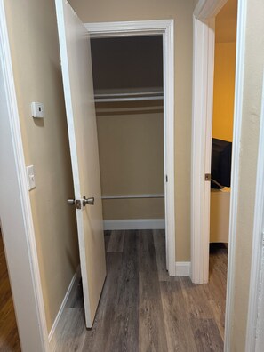 Ein begehbarer Kleiderschrank mit einer teilweise geöffneten Tür, durch die ein Holzboden und ein Bereich zum Aufhängen von Kleidung zu sehen sind.
