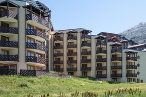 A multi-story hotel with balconies, a grassy area in front, and a mountainous backdrop. - Wifi, 10m from ski slopes, sauna, hammam, ski locker, 28-30m², Val Thorens (Val Thorens)