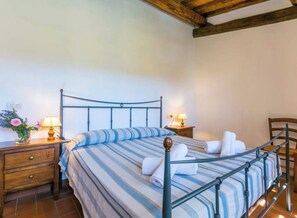 Ein Einzelbett mit Metallgestell, ein Nachttisch aus Holz mit einer Lampe und ein Holzstuhl.