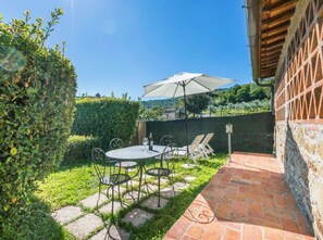 An outdoor patio with a table and chairs, a large umbrella, and a stone pathway. - Vigna Sweet Home – The Essence of the Tuscan Hills (Lucolena In Chianti)