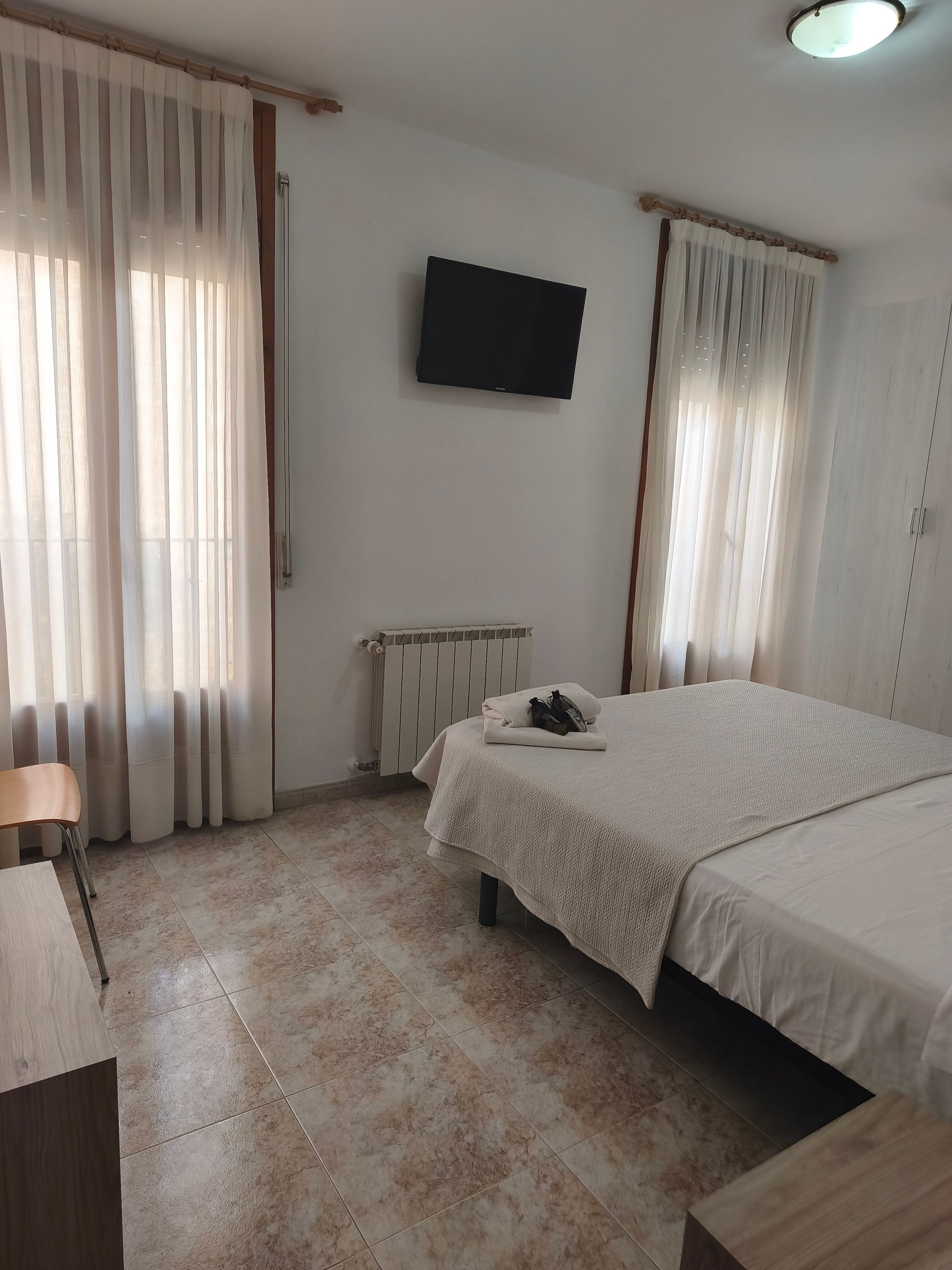 Una habitación de hotel con una cama, una silla, un televisor y un radiador.