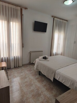 Una camera d'albergo con un letto, una sedia, una televisione e un termosifone.