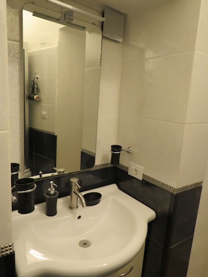 A bathroom with a white sink, black fixtures, and a mirror. - Essential and central apartment (Palermo)