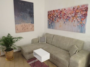 A living room with a beige sofa, a white side table, a potted plant, and two wall art pieces. - Essential and central apartment (Palermo)