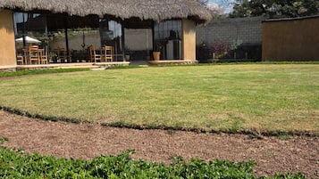 Un edificio con techo de paja, asientos al aire libre y un césped bien cuidado.