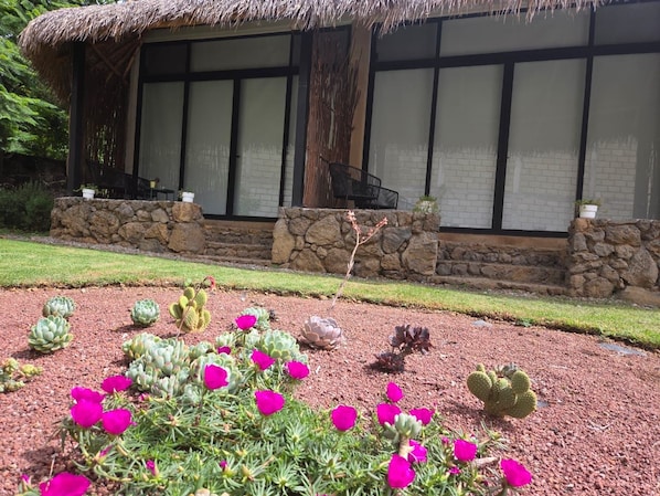 A building with a thatched roof, stone walls, and a garden with various plants and flowers.