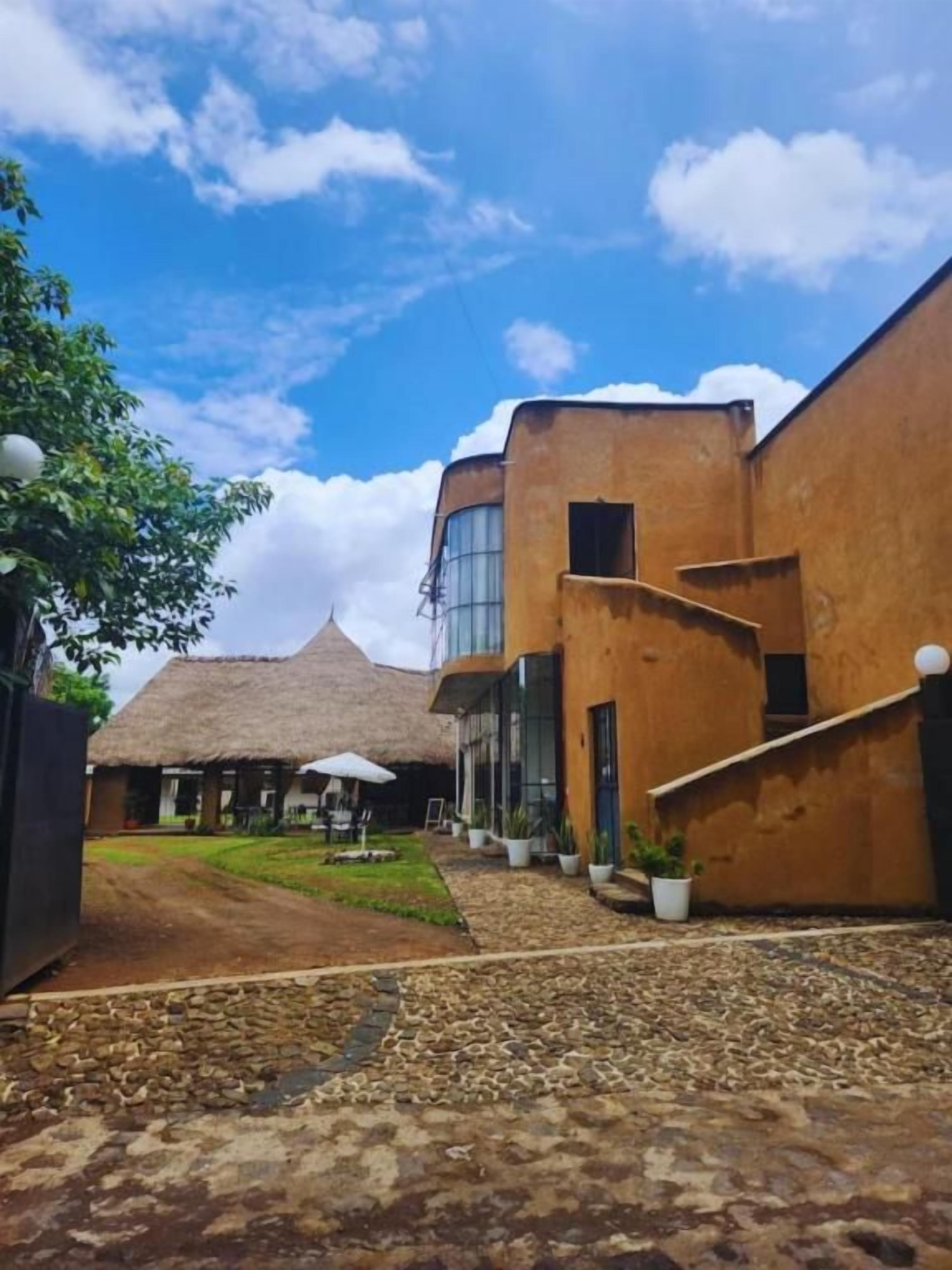 A courtyard with a thatched-roof building, a modern structure with large windows, and potted plants.