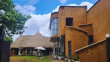 A courtyard with a thatched-roof building, a modern structure with large windows, and potted plants.
