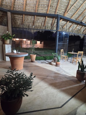 An indoor patio area with a thatched roof, potted plants, and seating arrangements.