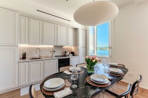 Une cuisine moderne avec des meubles blancs, une table à manger pour quatre personnes et une grande fenêtre donnant sur un beau paysage.