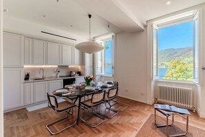 A modern kitchen with white cabinetry, a dining table with chairs, and a view of a lake through large windows. - Daydream in Villa Pozzi by MyHomeInComo (Blevio)