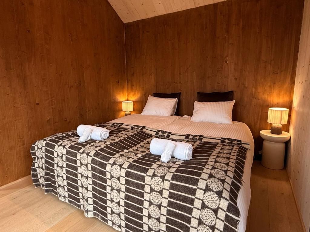 A wooden-paneled room with a bed, two bedside lamps, and towels on the bed.