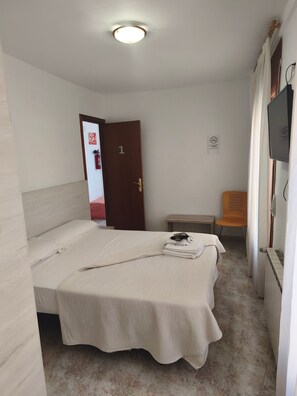 Een kamer met een bed, een stoel, een televisie en een deur met een nummer.