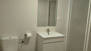 Un baño con inodoro, lavamanos, espejo y zona de ducha.