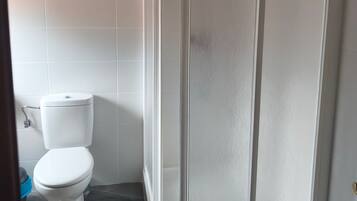 Un baño con inodoro blanco, cabina de ducha y paredes con azulejos.