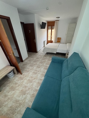Una habitación con cama, sofá, televisión y ventana con cortinas.