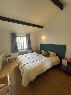 Une chambre à coucher avec un lit, une chaise, une table de chevet, une lampe et une fenêtre avec des rideaux.