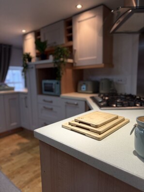 A modern kitchen with a countertop, wooden cutting boards, a microwave, and a stove. - Cosy, modern top floor apartment, in the heart of Montrose (Angus)