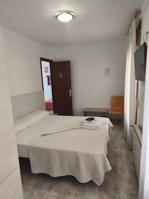 Een kamer met een bed, een stoel, een televisie en een deur met een nummer.