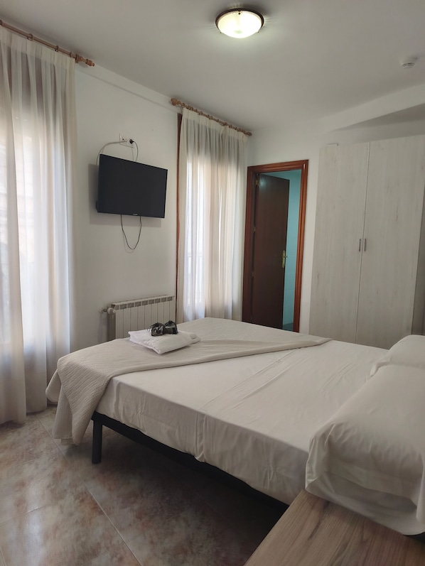 Een hotelkamer met een bed, een aan de muur bevestigde televisie, een kledingkast en een deur.