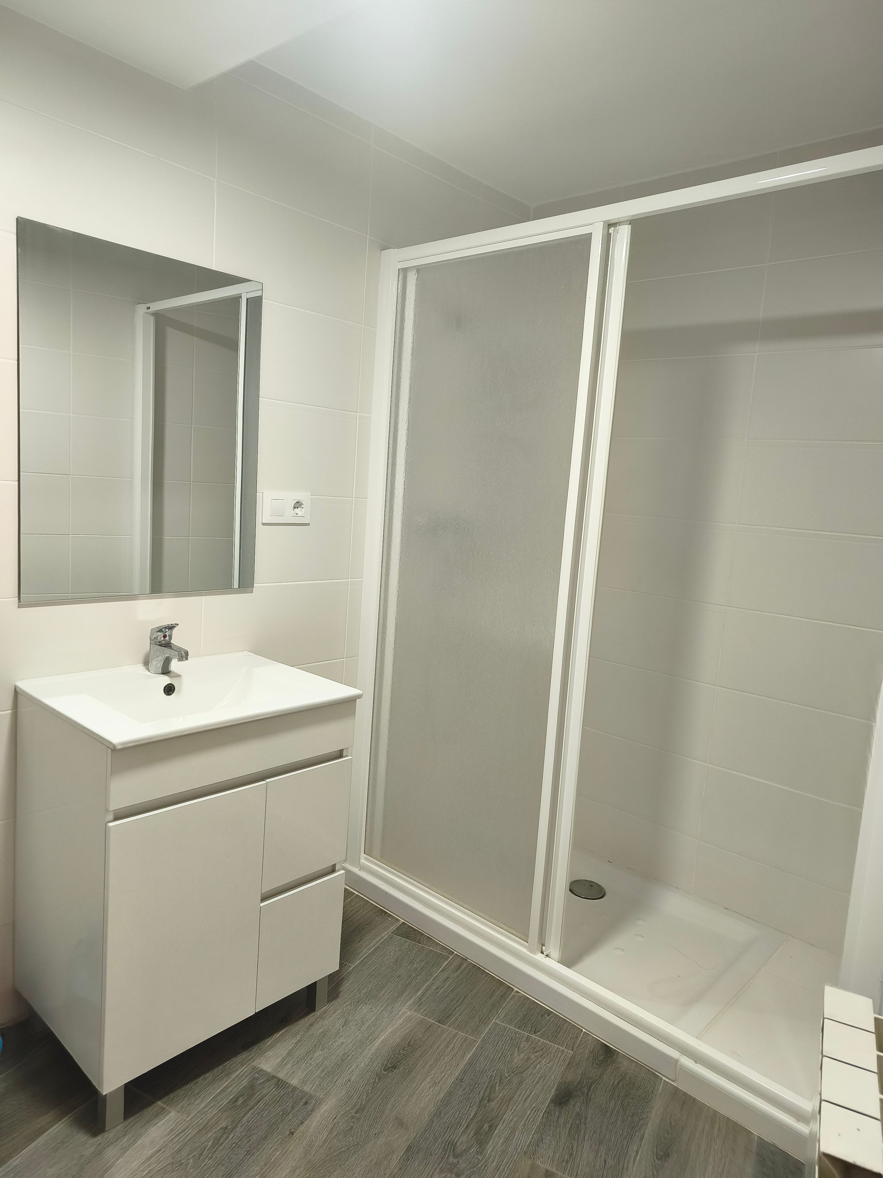 Un baño con tocador blanco, espejo y cabina de ducha con mampara de vidrio.