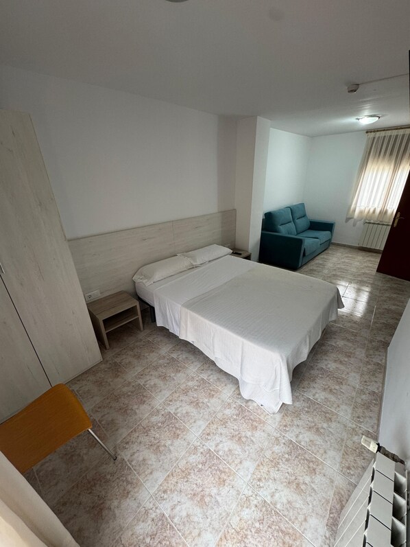 Una camera da letto con un letto, un comodino, una sedia, un divano e un termosifone.
