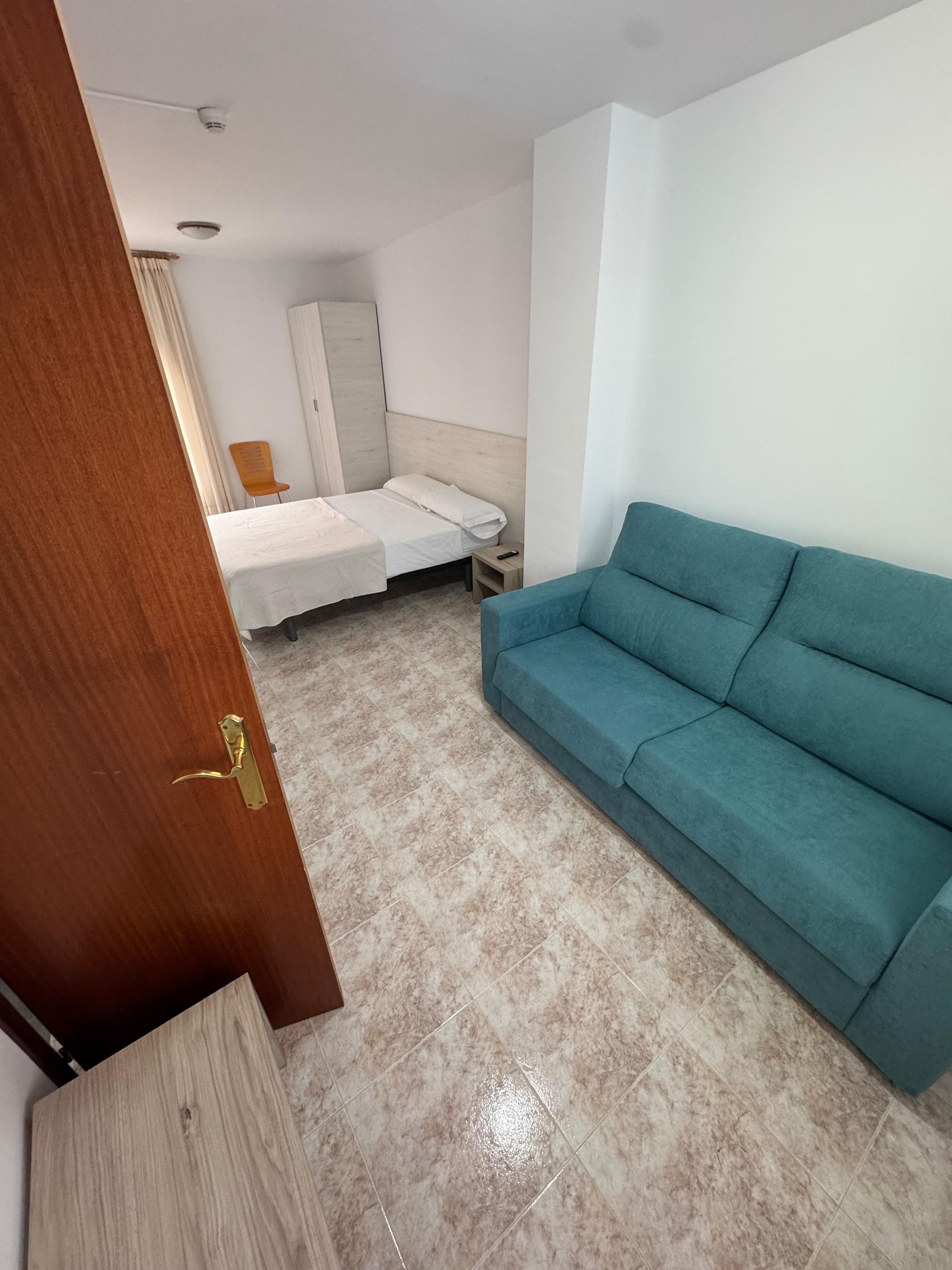 Habitación de hotel con cama, sofá azul, puerta de madera y suelo de baldosas.