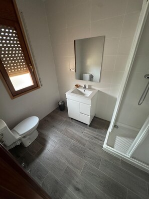 Un baño con inodoro, lavamanos, espejo y ducha.
