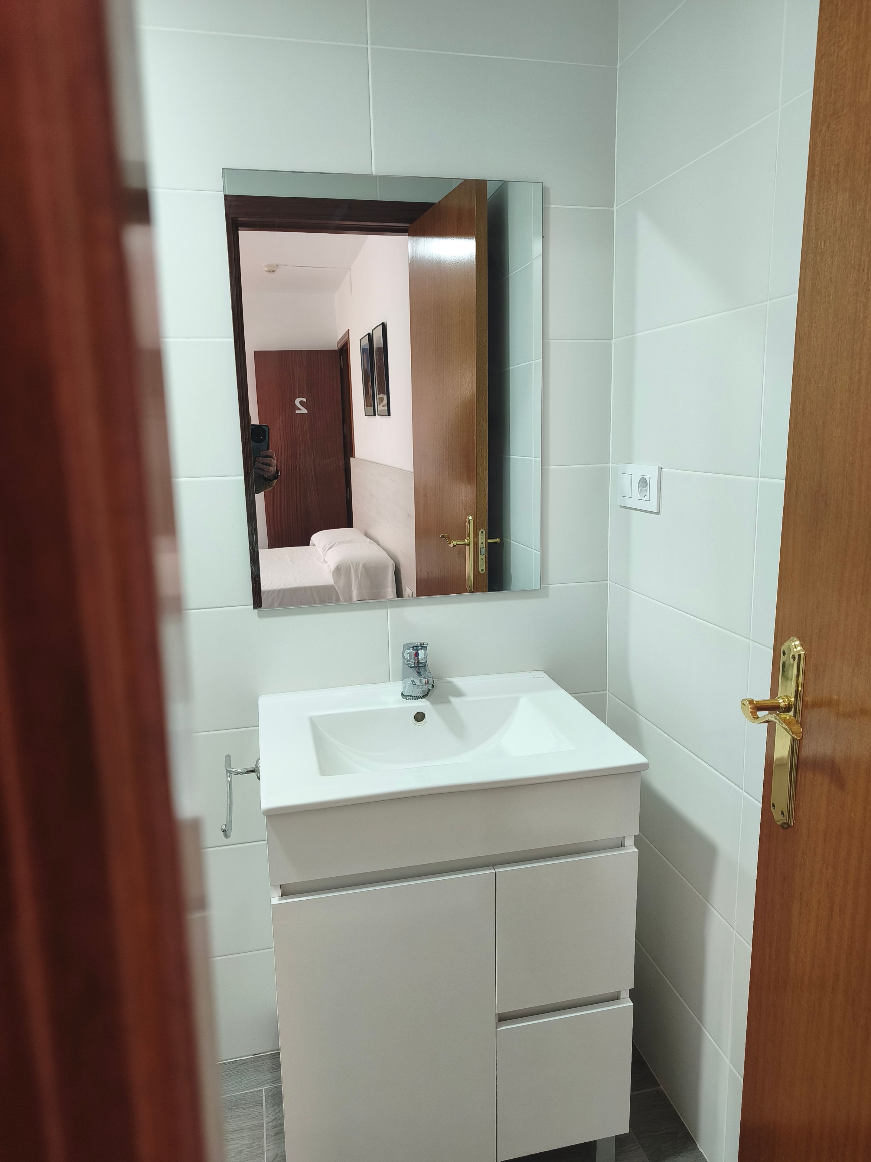 Un baño con un lavamanos blanco, un espejo y una puerta de madera.