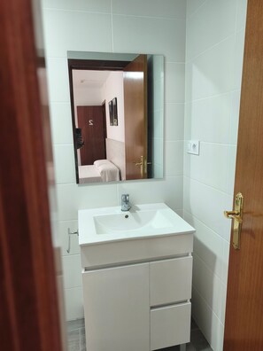 Een badkamer met een wit wastafelmeubel, een spiegel en een houten deur.