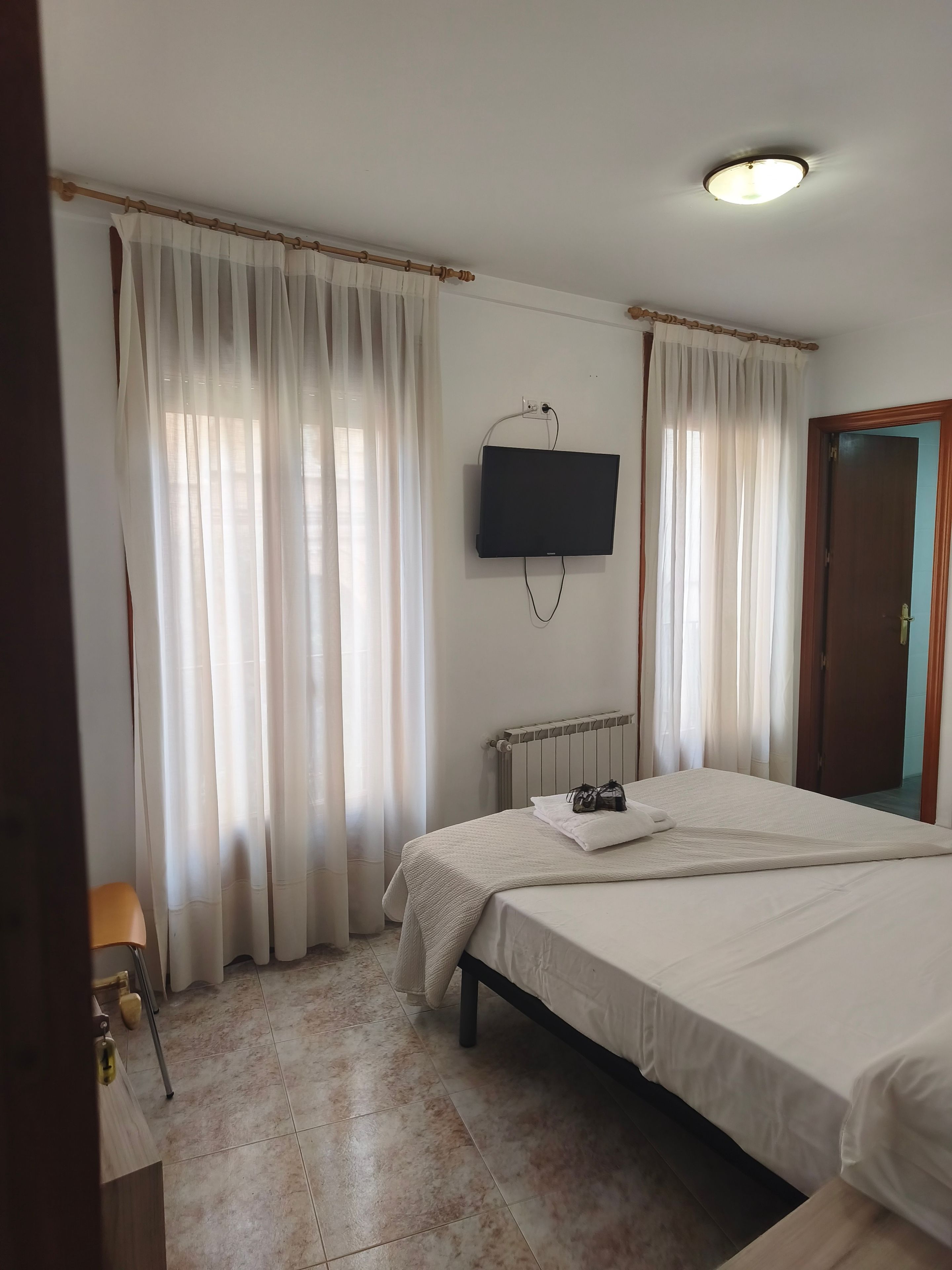 Habitación de hotel con cama, televisor montado en la pared y ventana con cortinas.