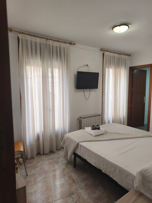 Una camera d'albergo con un letto, una televisione a muro e una finestra con tende.