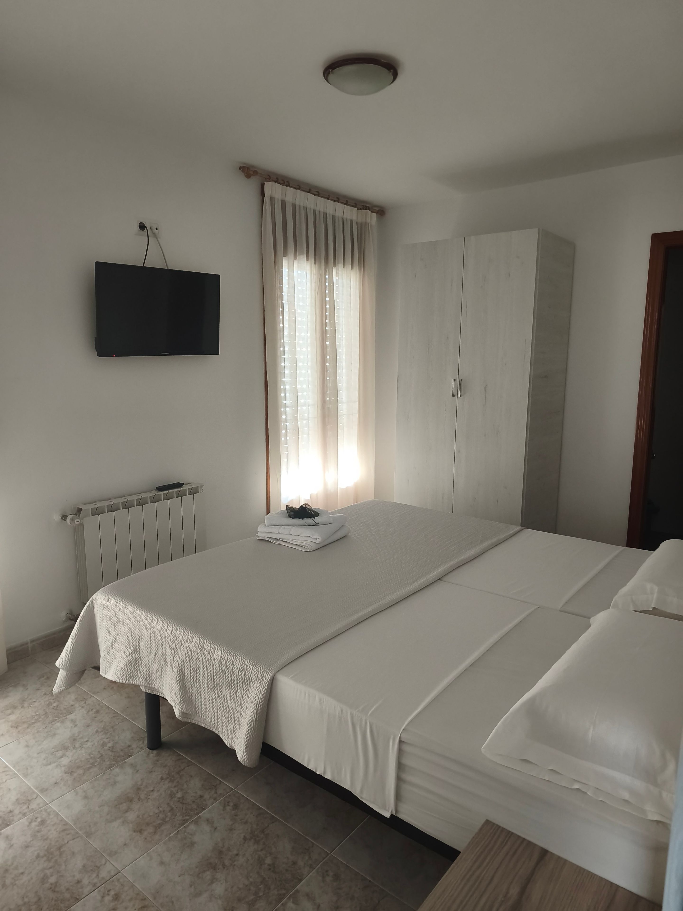 Un dormitorio con cama, armario, radiador y televisor montado en la pared.