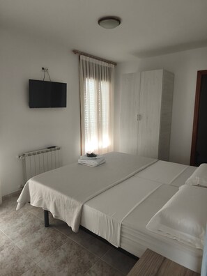 Een slaapkamer met een bed, een kledingkast, een radiator en een aan de muur bevestigde televisie.