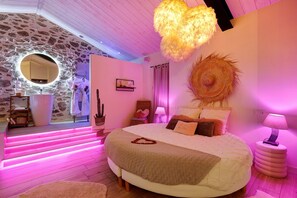A bedroom with a large bed, a round mirror, and a wall-mounted light fixture.