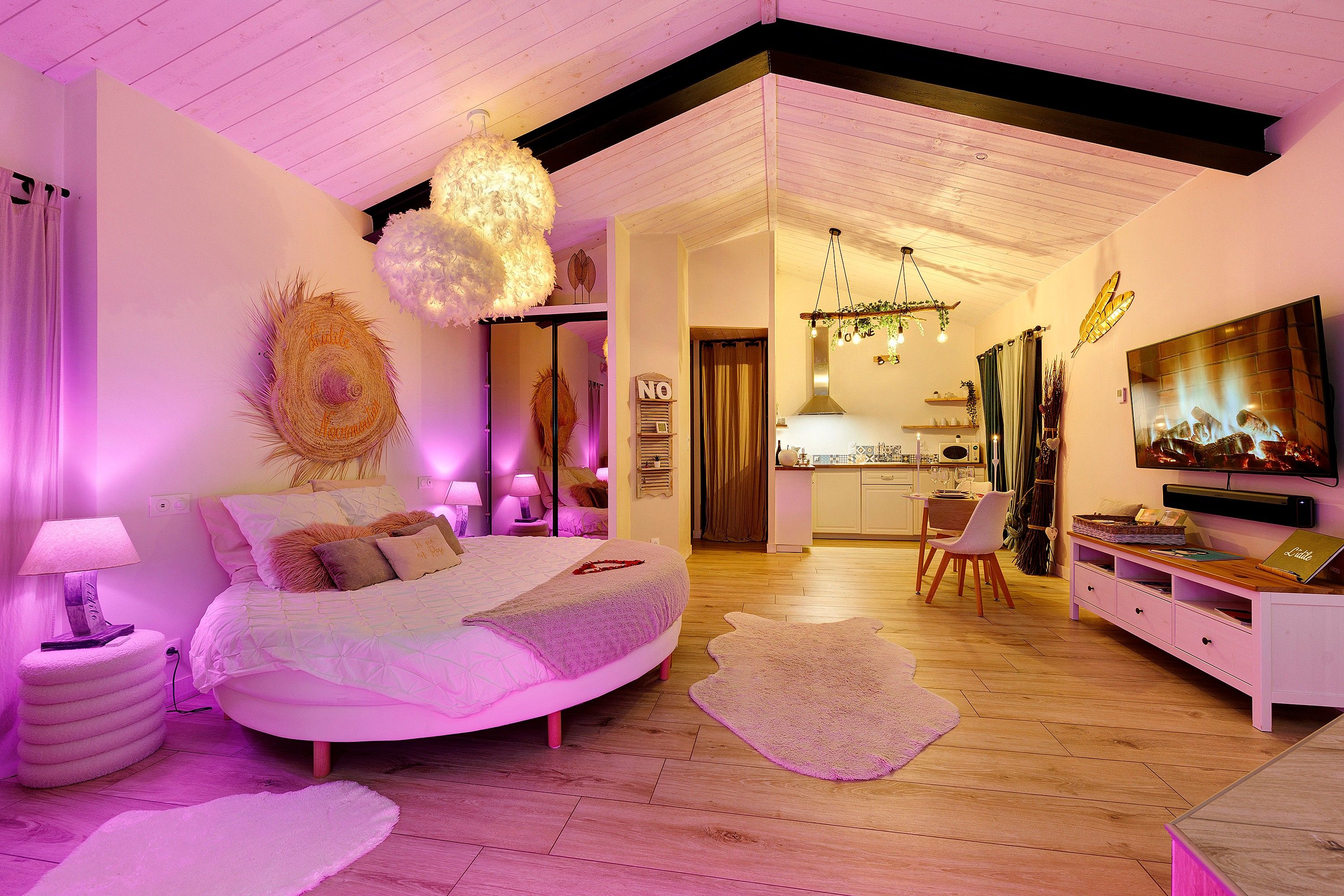 A modern bedroom with a curved bed, a dining area, and a kitchen.