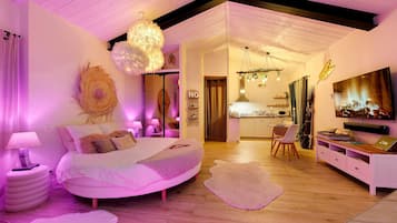 A modern bedroom with a curved bed, a dining area, and a kitchen.