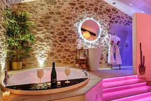 A bathroom with a stone wall, a round mirror, a bathtub, and a plant.