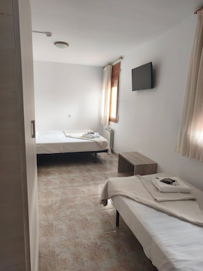 Een kamer met twee bedden, een televisie aan de muur en een raam met gordijnen.