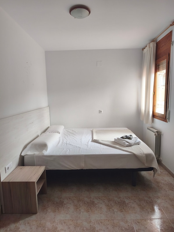 Een kleine eenpersoonskamer met een houten hoofdbord, nachtkastje en een radiator.