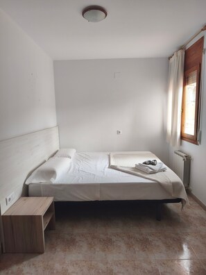 Una stanza piccola con un letto singolo, una testiera in legno, un comodino e un termosifone.